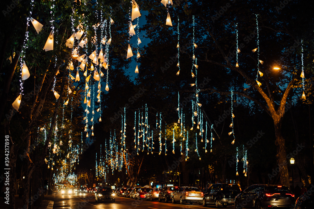 European street decorated for Christmas celebration. Avenida da Liberdade in Lisbon illuminated with lights hanging from the trees. Traffic on the road in Christmas night