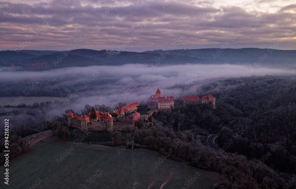 Fototapeta premium Aerial view of the large and beautiful Moravian royal castle Veveri (Burg Eichhorn), standing on a rock above water dam on the river Svratka, early morning light and autumn weather with the green fore