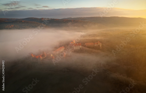 Aerial view of the large and beautiful Moravian royal castle Veveri (Burg Eichhorn), standing on a rock above water dam on the river Svratka, early morning light and autumn weather with the forest