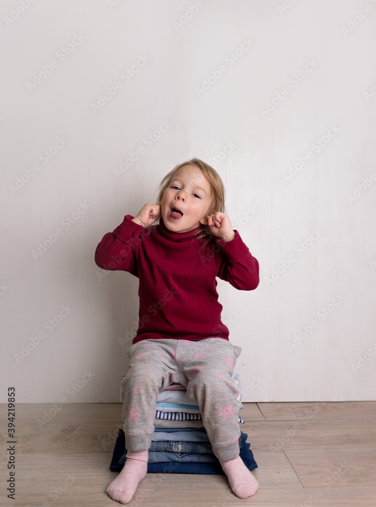 A cute little girl in a red sweater is sitting and showing her tongue on a pile of folded clothes