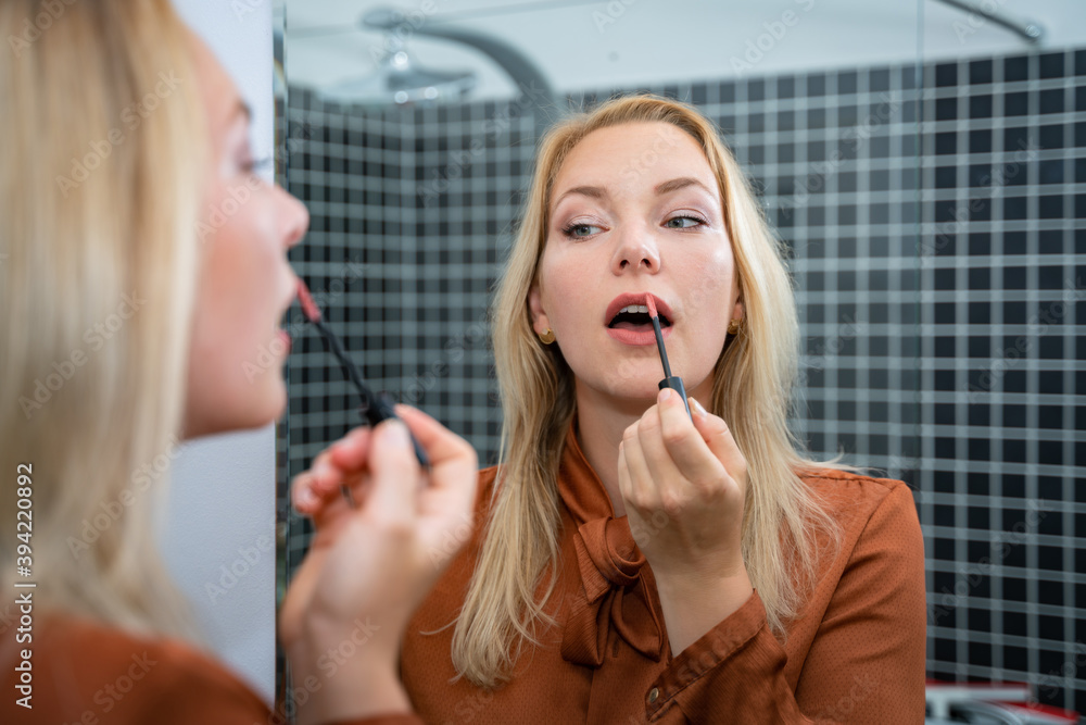 Fototapeta premium Make-Up, junge Frau zieht sich vor einem Spiegel die Lippen nach - Symbolfoto