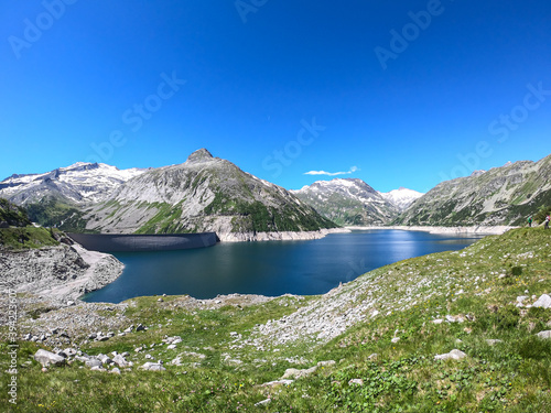 A panoramic view on an artificial, dam lake stretching over a vast territory around Alps in Austria. Lake is shining with navy blue color. In the back there are a few glaciers. Controlling the nature