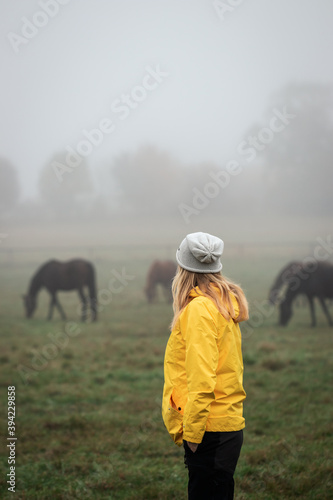 Woman enjoying view to horse at pasture in autumn foggy morning