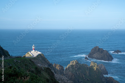 Cabo Ortegal lighthouse in Galicia with green cliffs and sunlight and deep blue ocean