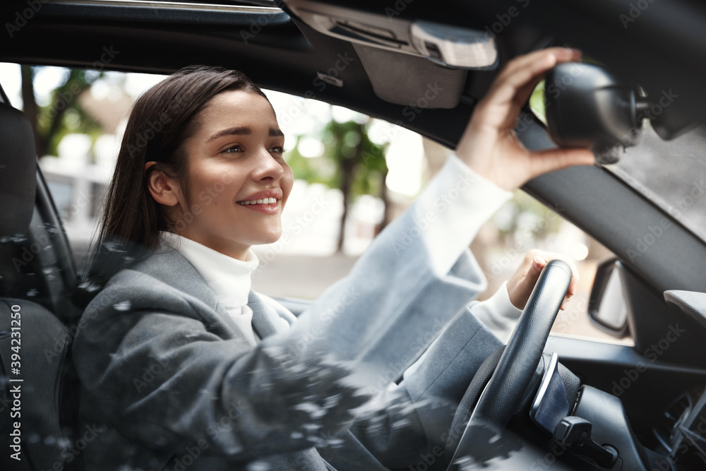 Elegant businesswoman looking at rear mirror, adjusting it for driving. Female executive drive her car and looking happy