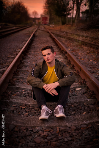 A young man sitting on the railways and looking forward.