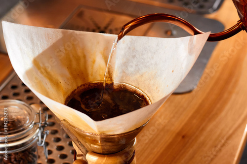 Making drip coffee. Barista pours hot water from a copper kettle through fresh ground coffee into the paper filter. Chemex. photo