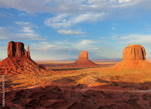 Fototapeta Naklejka Na Ścianę i Meble -  View To The East Mitten Butte, Merrick Butte And West Mitten Butte In The Monument Valley Arizona In The Late Afternoon Sun On A Sunny Summer Day With A Clear Blue Sky And A Few Clouds