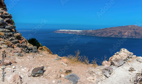 The rocky foreground of Skaros Rock in front of the caldera view towards Oia in summertime