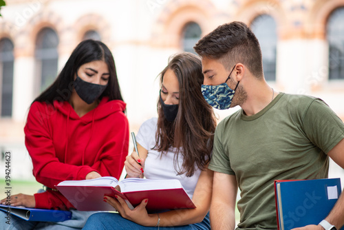 Students studying together sitting on a bench outdoor and wearing masks during coronavirus times