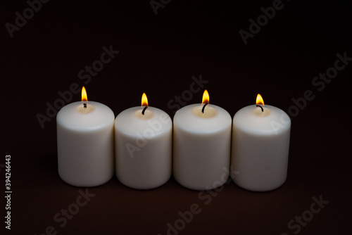 Four white candles flame burning on dark background with copy space for text.