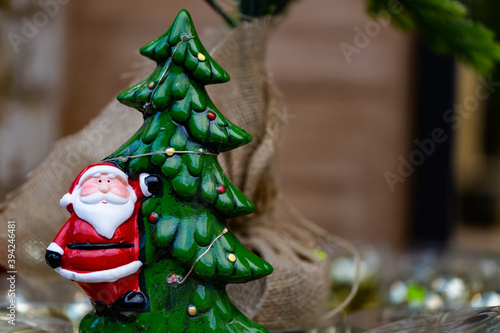 Santa Claus and Christmas tree flashes toy on blurred background. Merry Christmas and Happy new Year. Cute Santa Claus toy close up, copy space for text. Traditional santa claus
