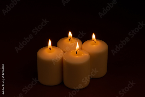 Four white candles flame burning on dark background with copy space for text.