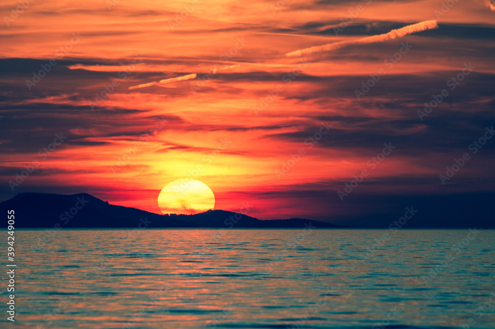 Big sun during beautiful sunset over the mountain on sea. Toned image