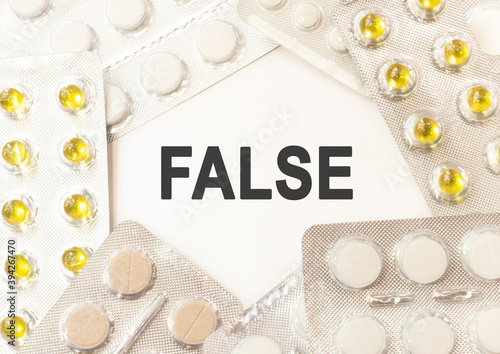 Text false on white background. There are various pills and vitamins around. Medicne concept photo