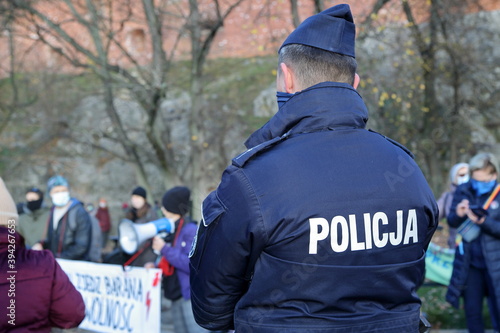 Polish policemen in blue uniform on his back stands in front of anti-government and anti-ruling party protesters in Krakow, November 2020