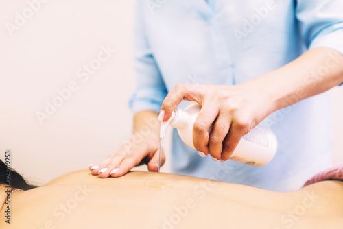 Masseur pours oil from a bottle on the back of a client in a beauty salon