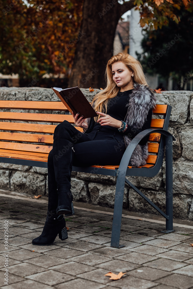 Portrait of a happy amazed woman reading a book while sitting on a bench in autumn park. Portrait of a happy amazed woman reading a book while sitting on a bench in autumn park.
