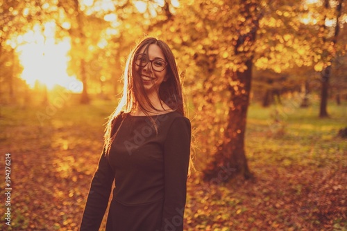 a young beautiful woman in the middle of a park surrounded by trees with autumn colors at sunset