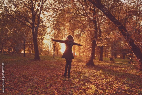 a young beautiful woman in the middle of a park surrounded by trees with autumn colors at sunset