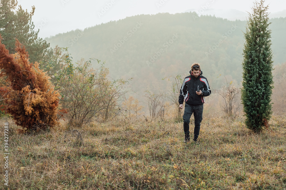 A young man uses a military compass for orientation in nature, talking on the phone, surrounded by fog.