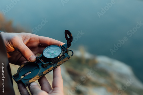 A young man uses a military compass for orientation in nature, talking on the phone, surrounded by fog.