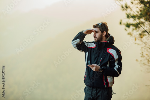 A young man uses a military compass for orientation in nature, talking on the phone, surrounded by fog.