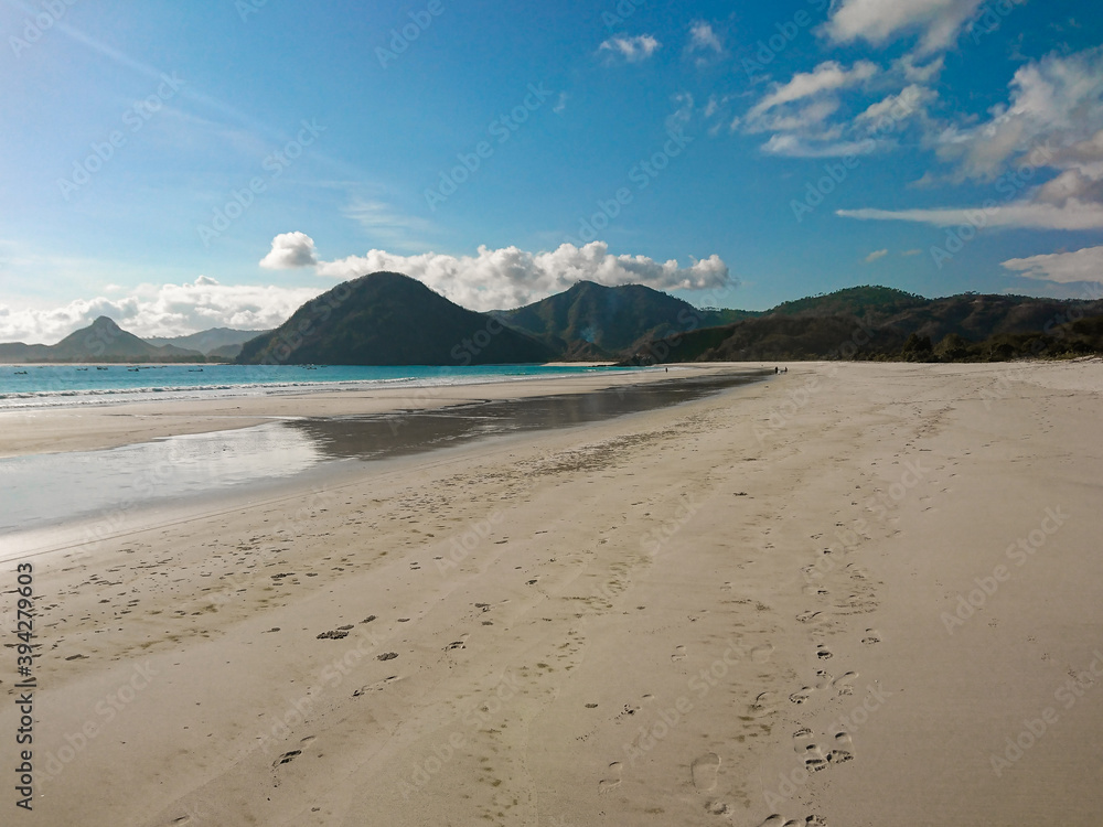 Pantai Selong Belanak, Lombok, West Nusa Tenggara, Indonesia: Image of a wide tropical sand beach on a beautiful summer day. Blue sky, beautiful clouds and wide mountain ranges in the background.