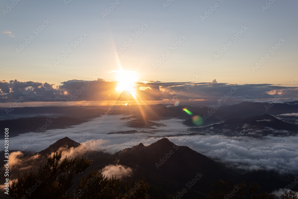 Mount Warning, New South Wales, Australia: Beautiful sunrise from the mountain top. Storm clouds forming sun rays and dense clouds covering the valleys of the volcano crater. Background image,