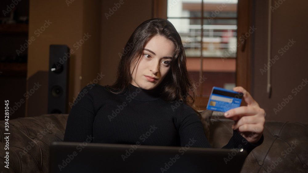 Beautiful sweet girl sitting on the sofa is shopping on her laptop and credit card in hand, shopping and technology concept Beautiful sweet girl sitting on the sofa is shopping on her laptop and credit card in hand, shopping and technology concept