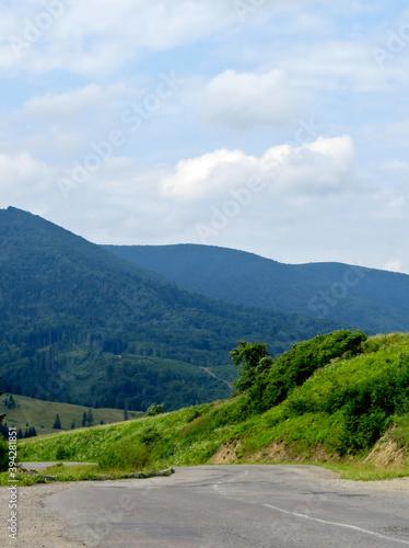 Mountain asphalt road on a background of mountains with green forests and bushes and blue sky with clouds