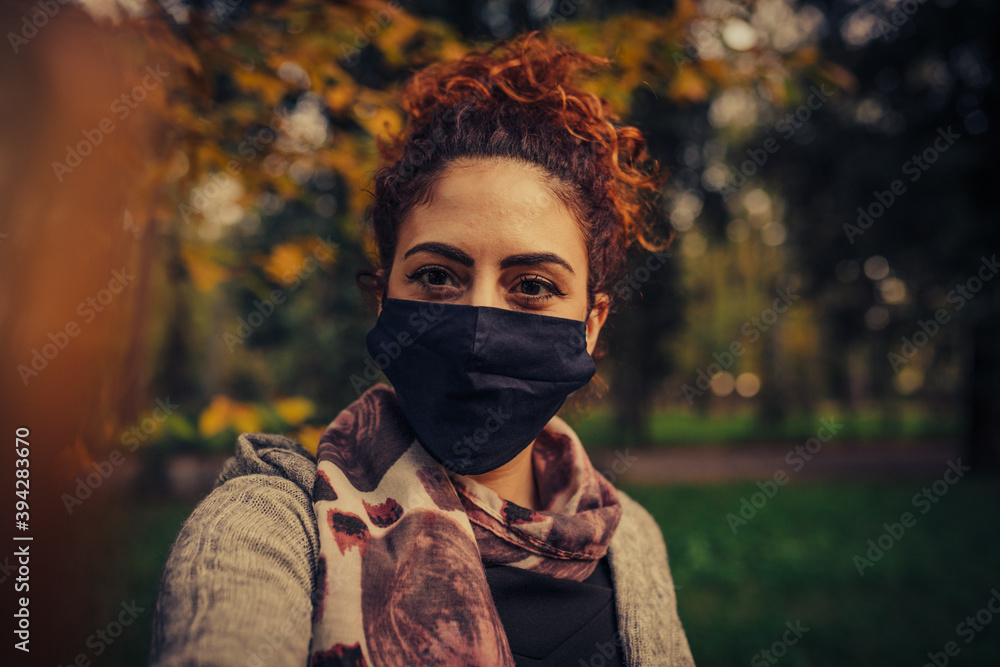 young red-haired woman wears a health mask while looking at another person in the middle of a park young red-haired woman wears a health mask while looking at another person in the middle of a park