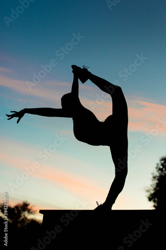 Girl acrobat at sunset doing stretching (yoga). Against the backdrop of beautiful clouds © Granmedia
