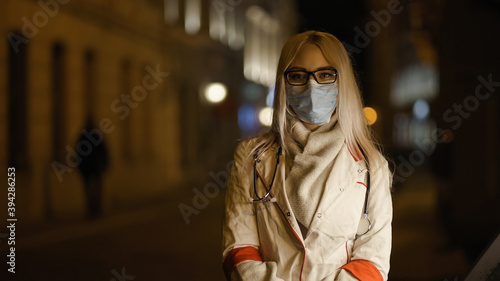 Serious medical intern looks at camera in front of hospital wearing medical mask