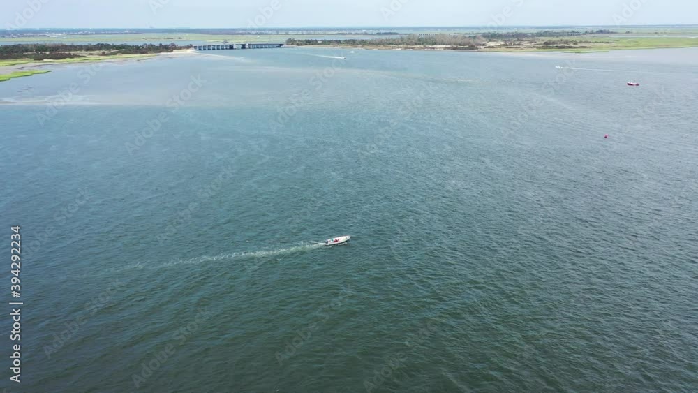 An aerial view over Jones Inlet on a sunny day. The camera truck right following a small boat from the side as it sails by on the calm waters below. An aerial view over Jones Inlet on a sunny day. The camera truck right following a small boat from the side as it sails by on the calm waters below.