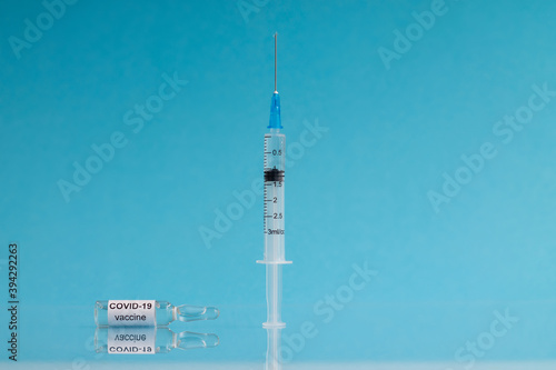 An ampoule with the COVID-19 coronavirus vaccine and a syringe stands against a blue background. Copy space