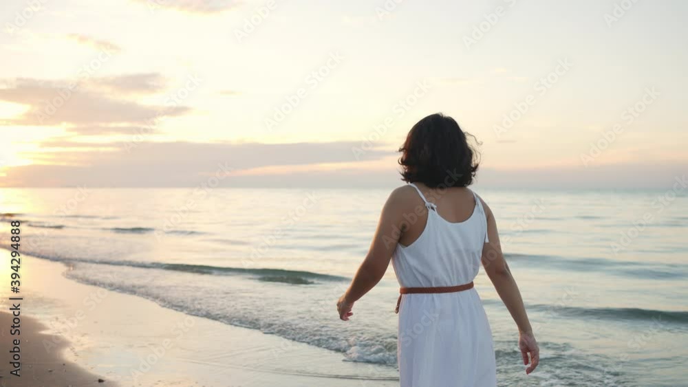 4K Happy beautiful Asian woman in white dress walking on tropical island beach on island beach in summertime at sunrise. Smiling woman relax and enjoy outdoor lifestyle in summer holiday vacation. 4K Happy beautiful Asian woman in white dress walking on tropical island beach on island beach in summertime at sunrise. Smiling woman relax and enjoy outdoor lifestyle in summer holiday vacation.