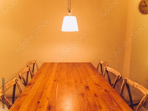 Wooden table and wooden chairs. A lamp hanging above the tabe and a clock on the wall. Toned image. photo