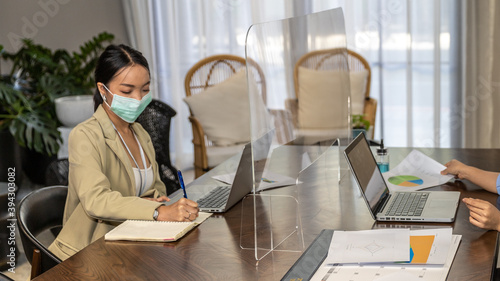 Female business workers with face mask having business discussion or agreement through transparent partition at the office as part of Business in New Normal during outbreak of COVID-19.