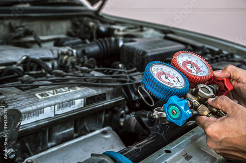 Close up hand of auto mechanic are to use measuring manifold gauge for filling car air conditioners. Concepts of fix and checking for repair service and car insurance.