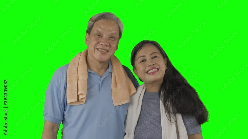 Elderly couple smiling at the camera while wearing sportswear and standing together in the studio with green screen background. Shot in 4k resolution Elderly couple smiling at the camera while wearing sportswear and standing together in the studio with green screen background. Shot in 4k resolution