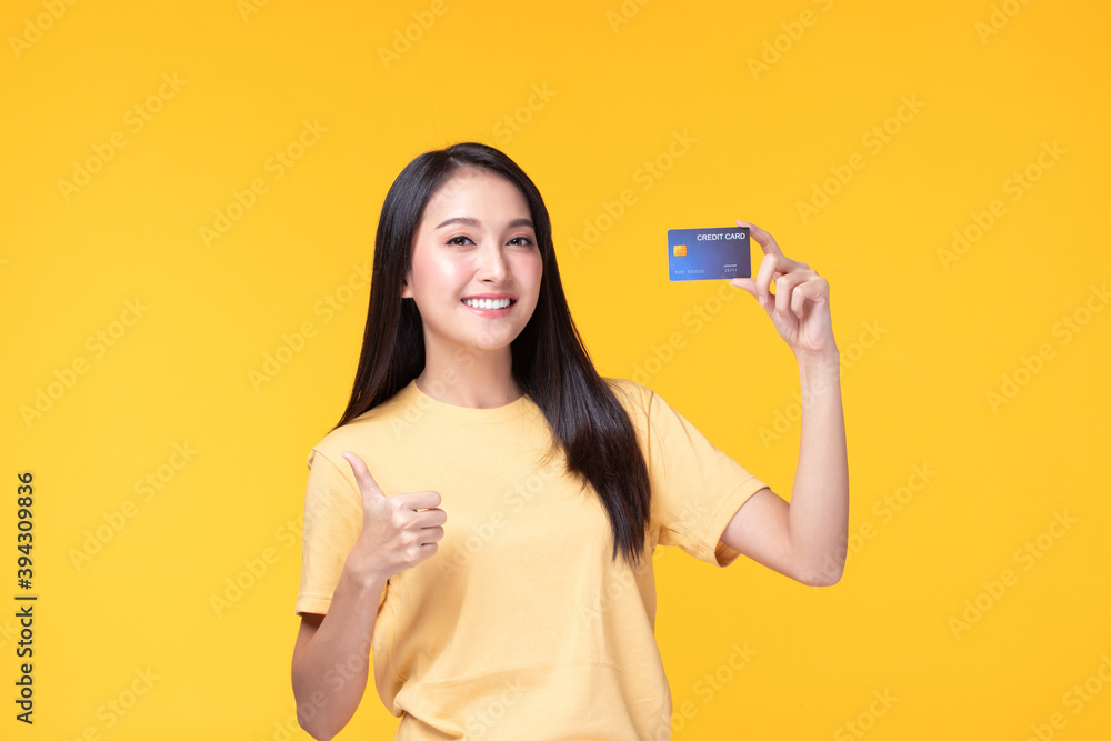 Cheerful young asian woman in yellow T-shirt holding bank card isolated on yellow background Cheerful young asian woman in yellow T-shirt holding bank card isolated on yellow background