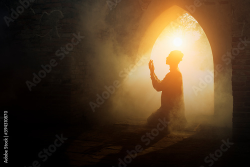 Fototapeta Silhouette religious of muslim male praying in old mosque with lighting and smok