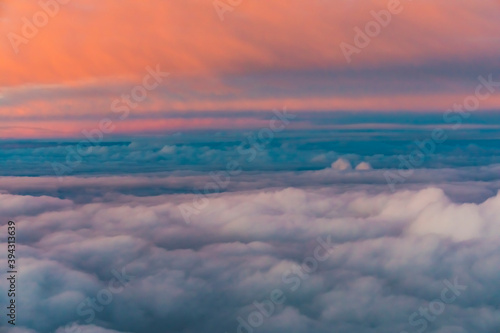 View of colorful fluffy clouds from an airplane at sunset, orange and teal cloudscape treatment