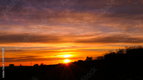 Amazing sunrise in rural scene. Dramatic sky with sunbeam and stratus clouds over the silhouette of hill on the horizon.