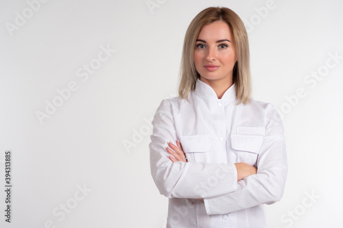 Portrait of a blonde in a white coat. Girl in a white uniform. Woman on a light background looks into the camera. Concept - a woman works in the field of cosmetology or medicine. Businesswoman