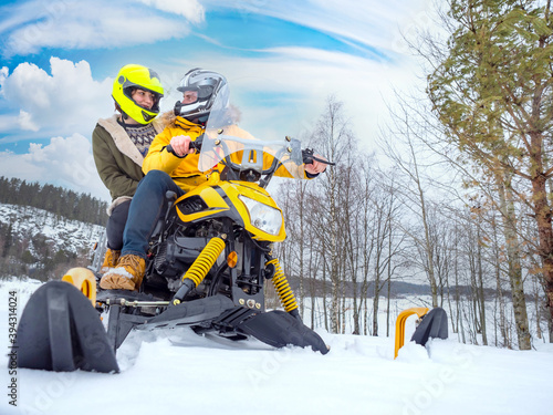Young couple on snowmobiling. Lovers ride a snowmobile. Snowmobile drivers look at each other. They are doing snowmobiling. Tourists snowmobiling in winter nature. Guy and a girl on yellow snowmobile