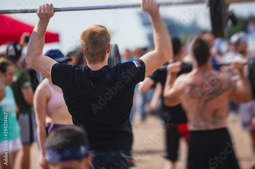 Process of group outdoor training  street workout on a summer sandy beach  with young muscular fit people exercising and lifting heavy weights  making cardio exercise  men and women working out