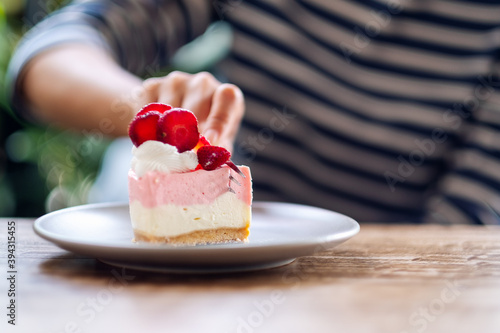 Closeup image of a woman eating a strawberry cheese cake in a plate