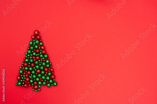 layout made of red and green shiny glitter balls laid out in the shape of a Christmas tree on a red background. Happy New Year concept. Creative minimalistic holiday concept. Top view with copy space